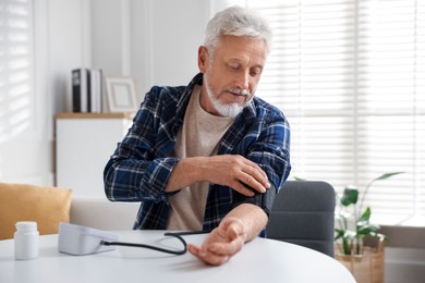 Photo of Senior man measuring blood pressure at table indoors