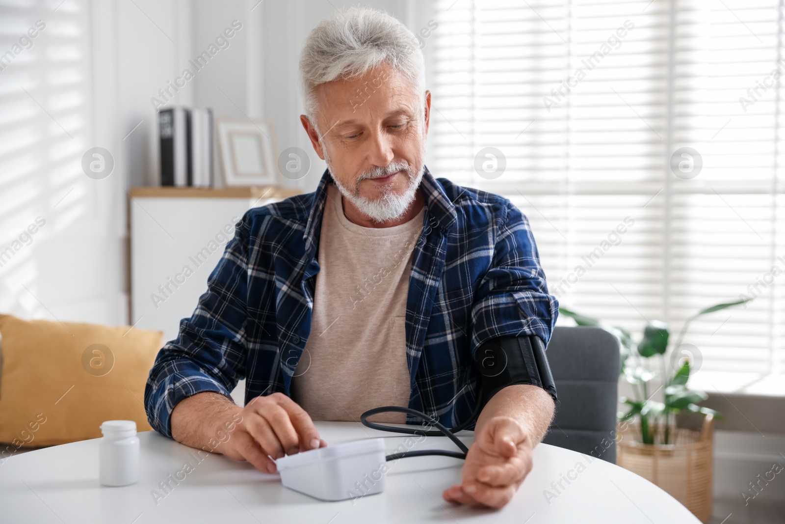 Photo of Senior man measuring blood pressure at table indoors