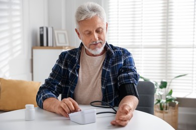 Photo of Senior man measuring blood pressure at table indoors