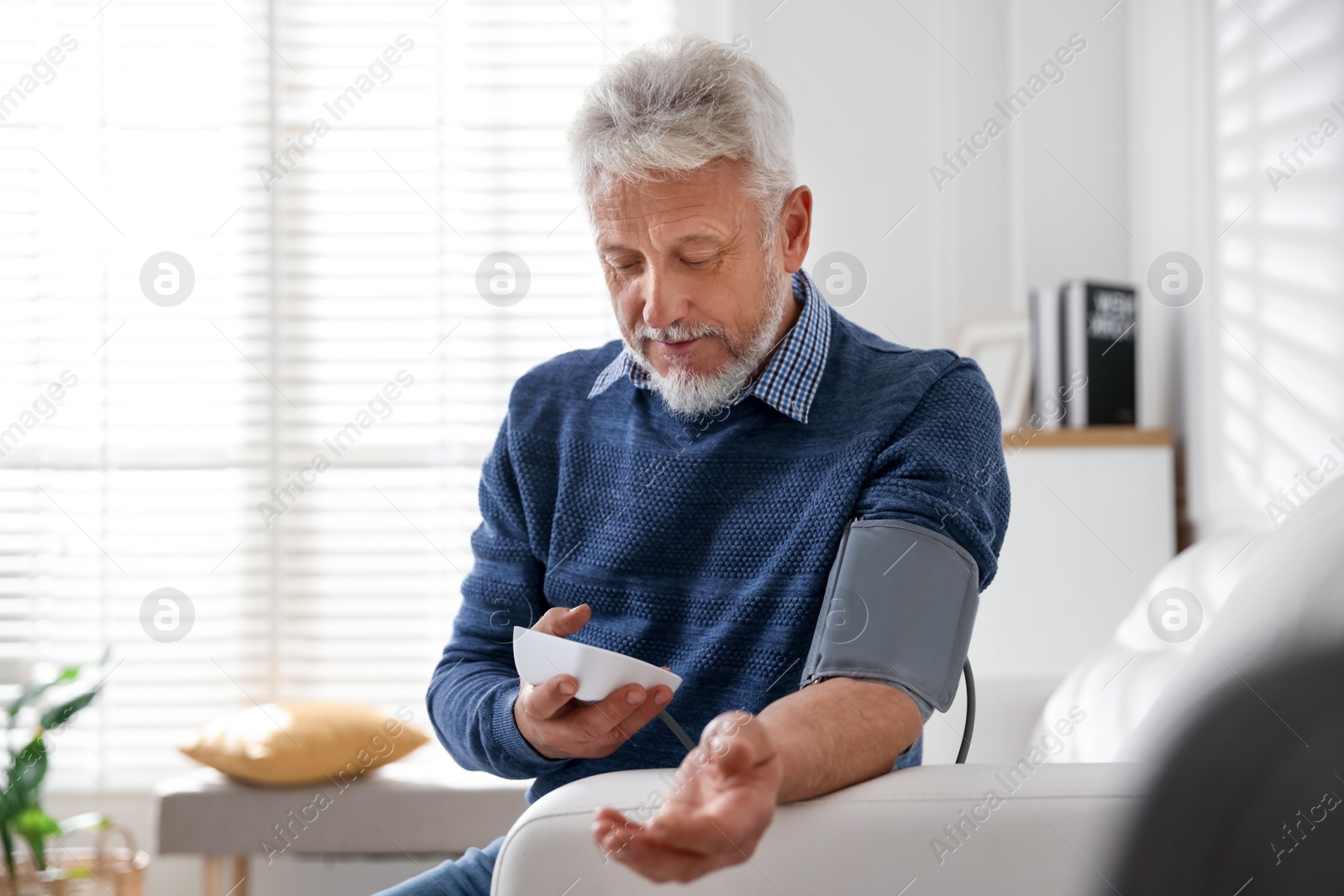 Photo of Senior man measuring blood pressure on sofa indoors