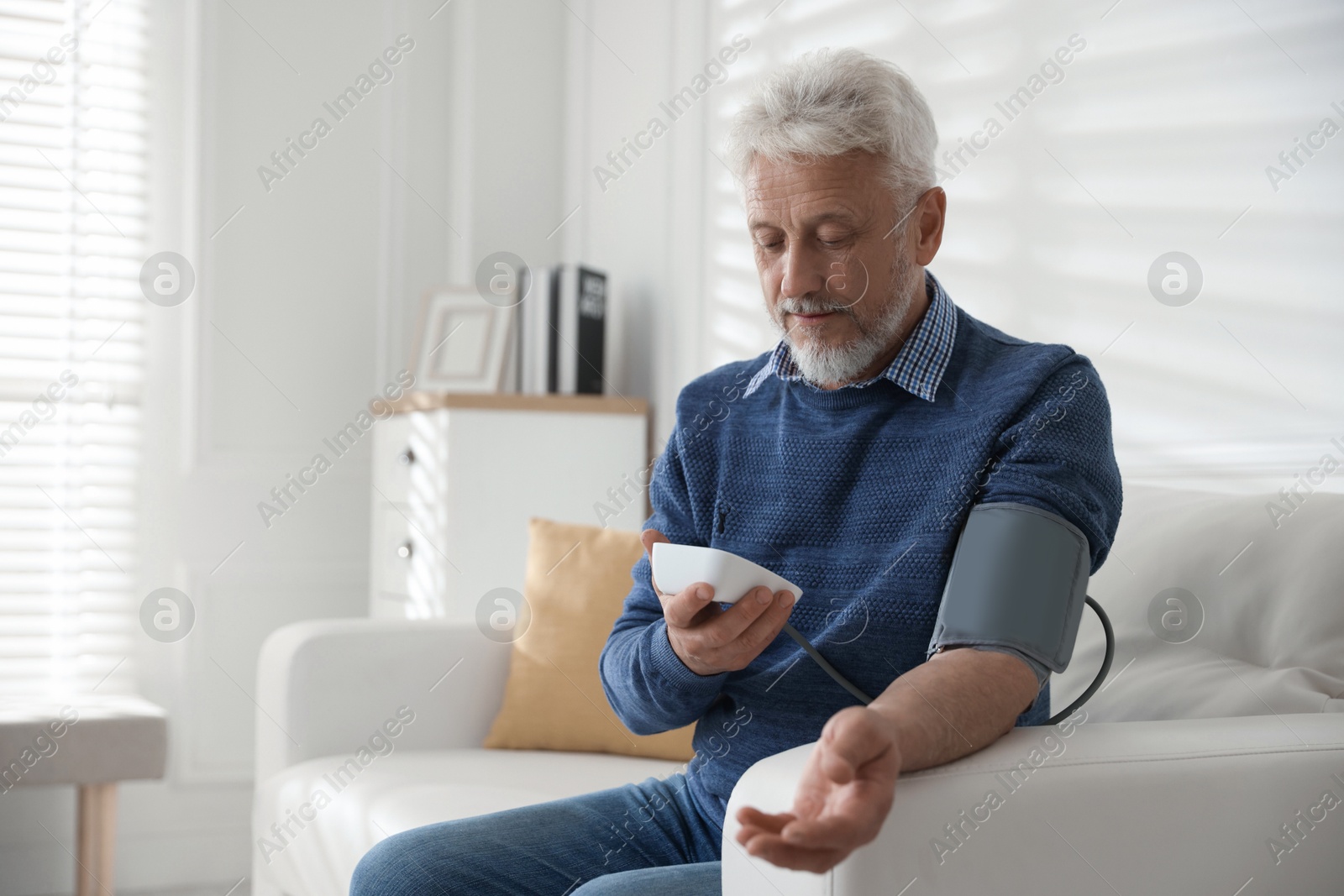 Photo of Senior man measuring blood pressure on sofa indoors