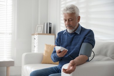 Photo of Senior man measuring blood pressure on sofa indoors