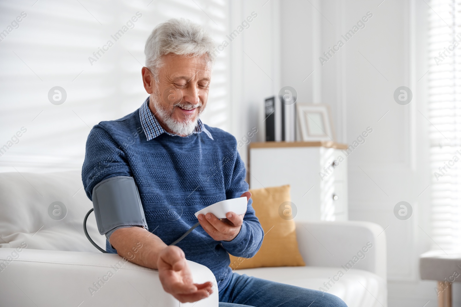 Photo of Senior man measuring blood pressure on sofa indoors