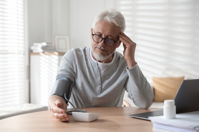 Photo of Senior man measuring blood pressure at table indoors