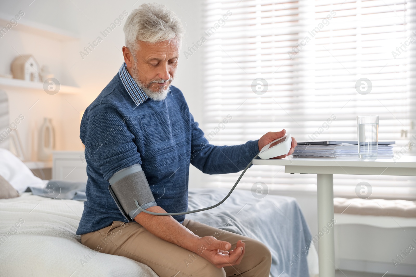 Photo of Senior man measuring blood pressure on bed indoors