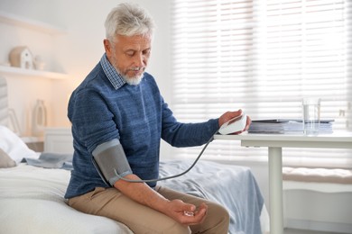 Photo of Senior man measuring blood pressure on bed indoors