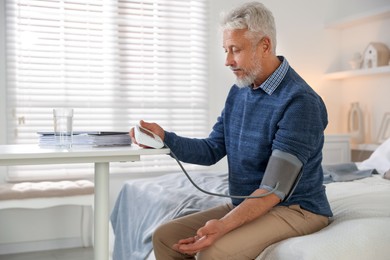 Photo of Senior man measuring blood pressure on bed indoors