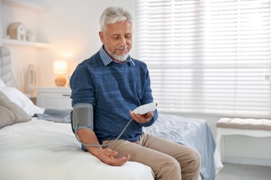 Photo of Senior man measuring blood pressure on bed indoors