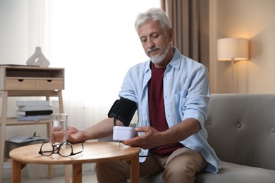 Photo of Senior man measuring blood pressure at table indoors