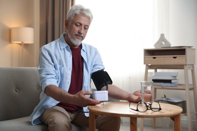 Photo of Senior man measuring blood pressure at table indoors