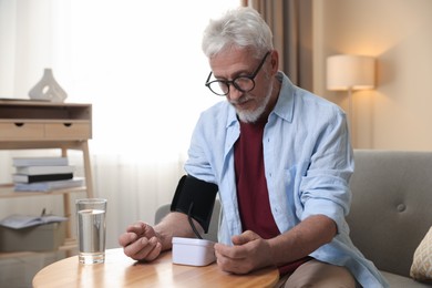 Photo of Senior man measuring blood pressure at table indoors