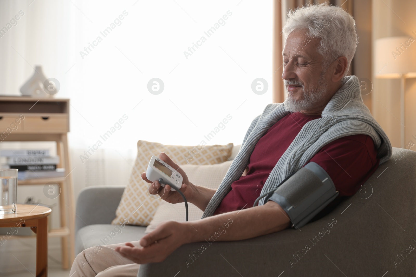 Photo of Senior man measuring blood pressure on sofa indoors