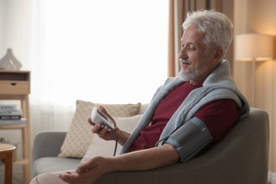 Photo of Senior man measuring blood pressure on sofa indoors