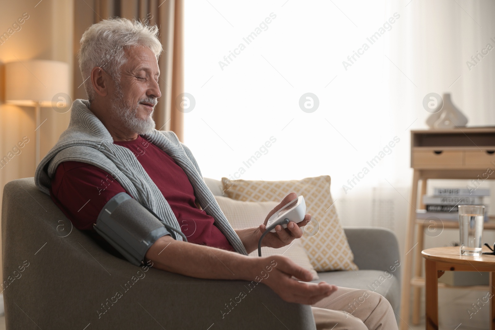 Photo of Senior man measuring blood pressure on sofa indoors