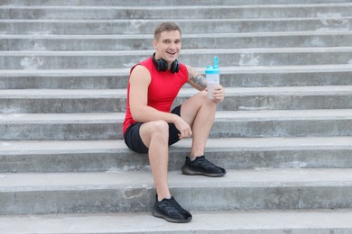 Photo of Smiling man with shaker of protein drink sitting on stairs outdoors