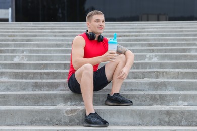 Photo of Athletic man with shaker of protein drink sitting on stairs outdoors