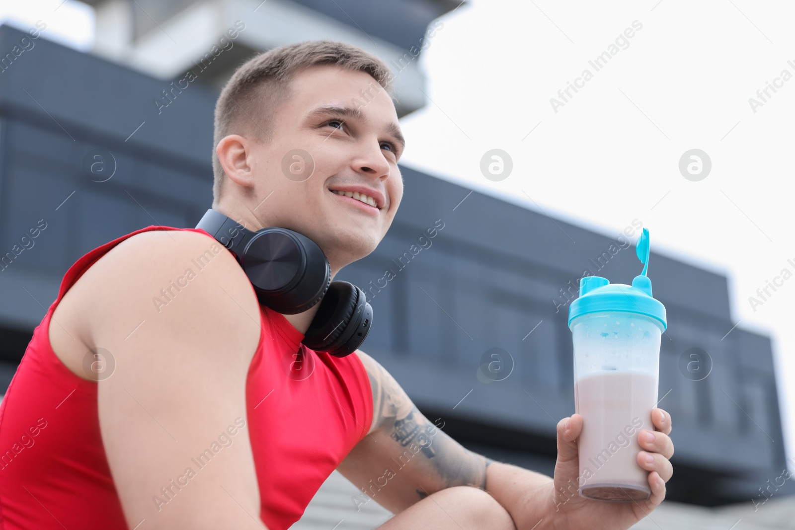 Photo of Smiling man with shaker of protein drink outdoors, low angle view