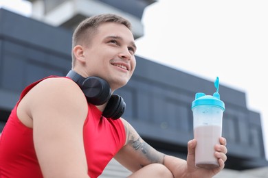 Photo of Smiling man with shaker of protein drink outdoors, low angle view