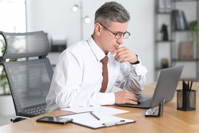 Photo of Businessman working on laptop at table in office