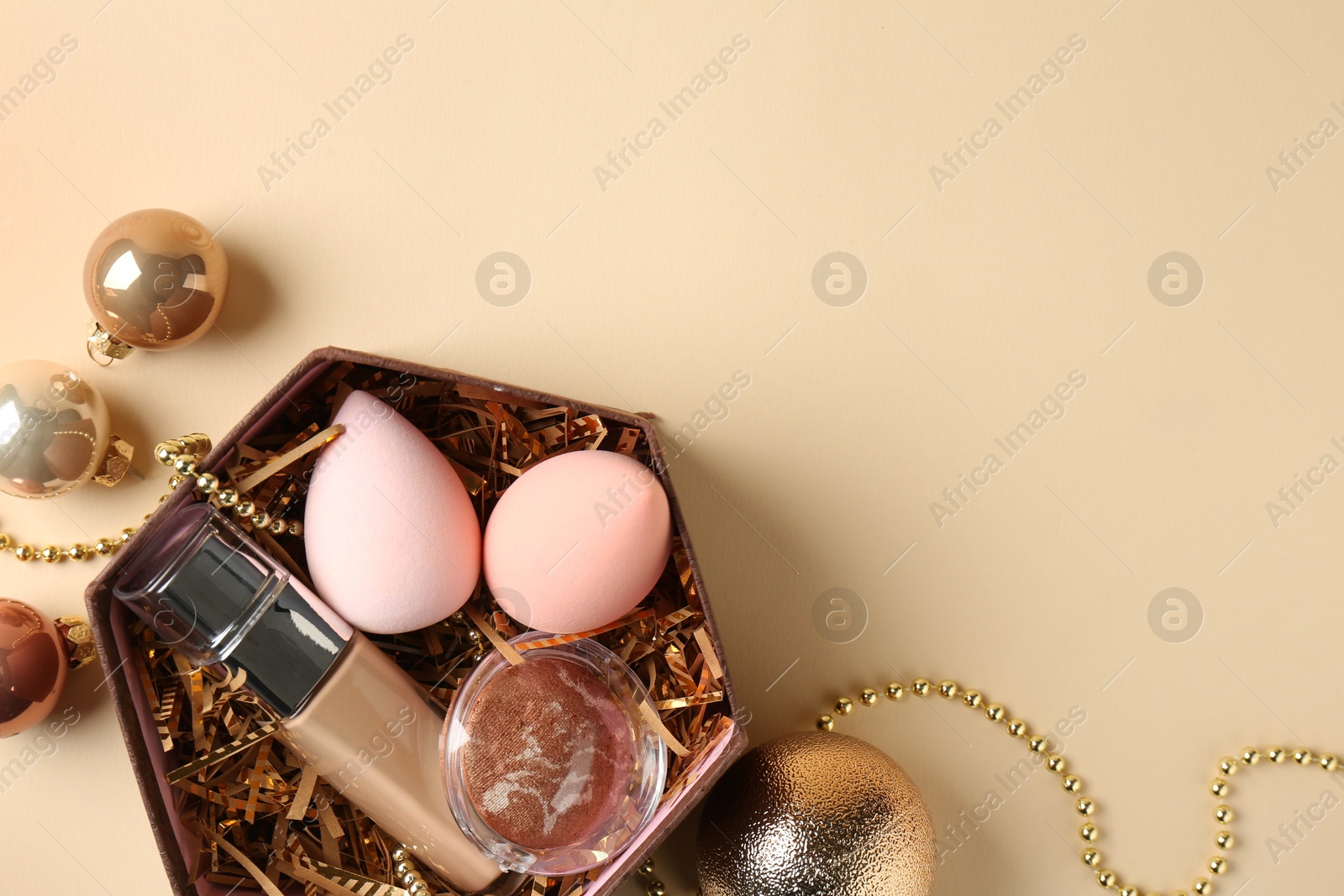 Photo of Cosmetic products in gift box and Christmas balls on beige background, flat lay. Space for text