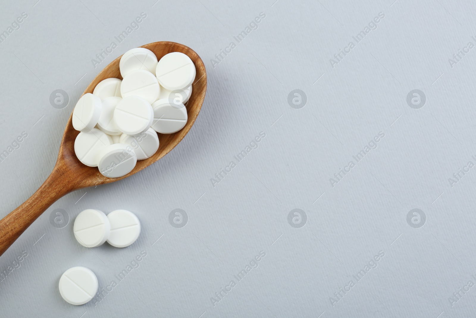 Photo of Antibiotic pills in wooden spoon on grey background, top view. Space for text