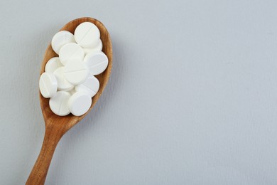 Photo of Antibiotic pills in wooden spoon on grey background, top view. Space for text