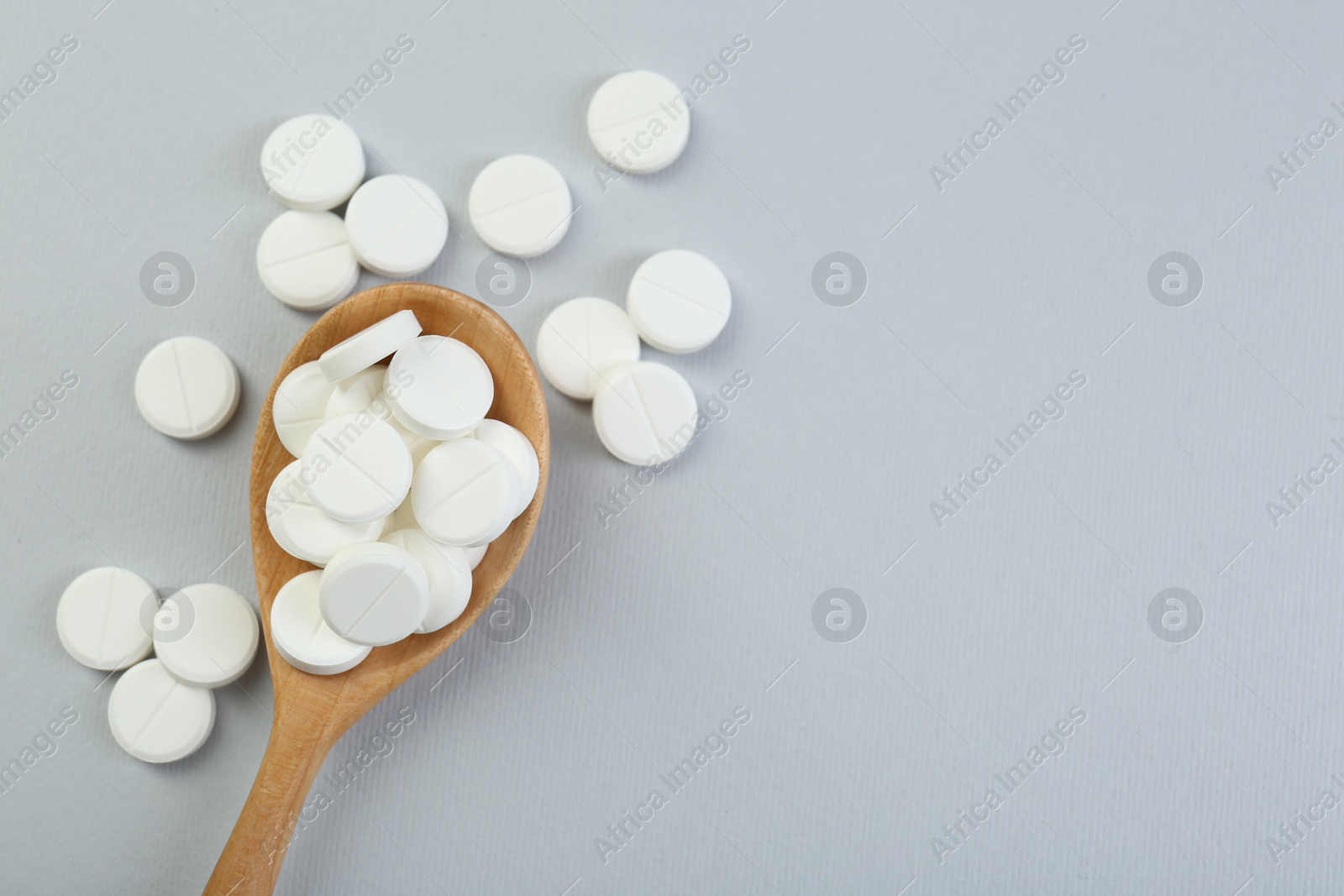 Photo of Antibiotic pills in wooden spoon on grey background, top view. Space for text