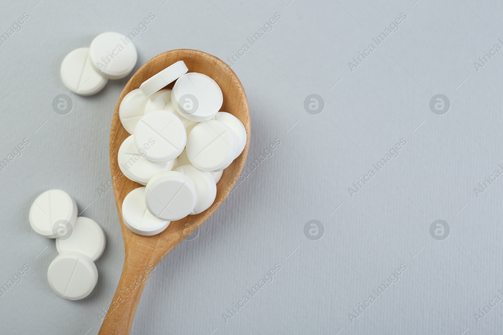 Photo of Antibiotic pills in wooden spoon on grey background, top view. Space for text