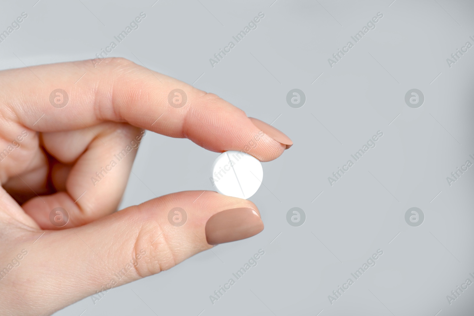 Photo of Woman holding antibiotic pill against grey background, closeup. Space for text