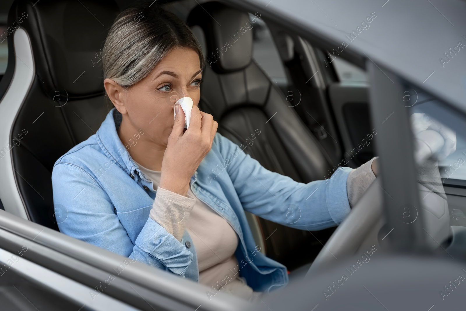 Photo of Woman with tissue blowing runny nose in car