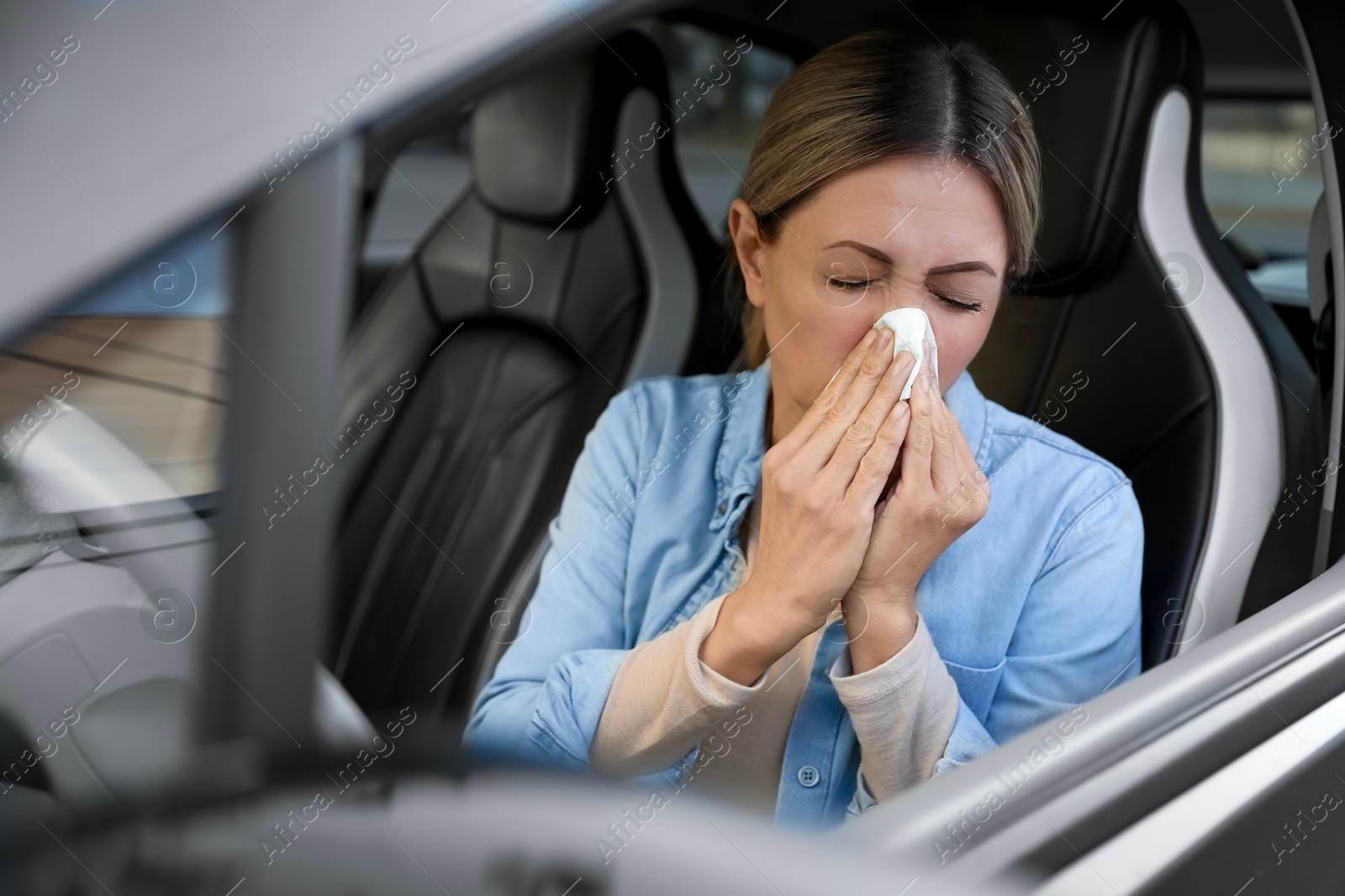 Photo of Woman with tissue blowing runny nose in car