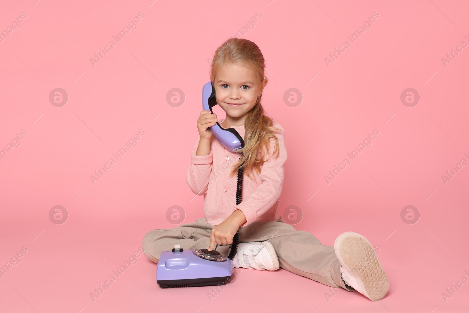 Photo of Cute little girl with telephone on pink background