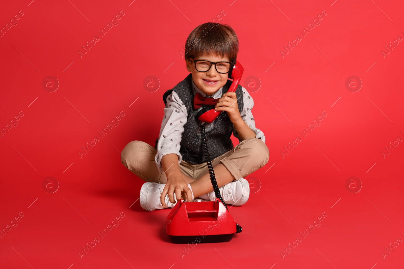 Photo of Cute little boy with old telephone on red background