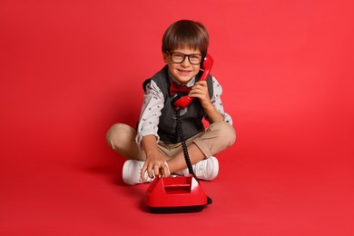 Cute little boy with old telephone on red background