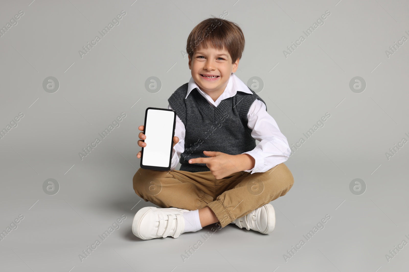 Photo of Cute little boy with smartphone on grey background