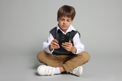 Photo of Cute little boy with smartphone on grey background