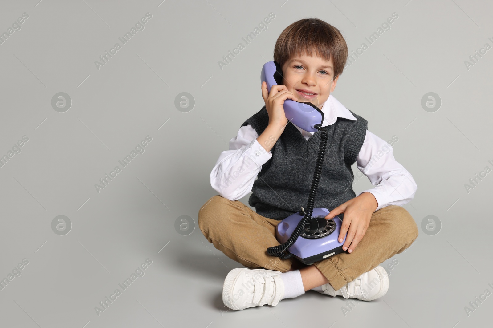 Photo of Cute little boy with old telephone on grey background, space for text