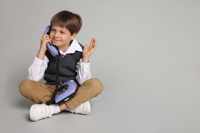 Cute little boy with old telephone on grey background, space for text