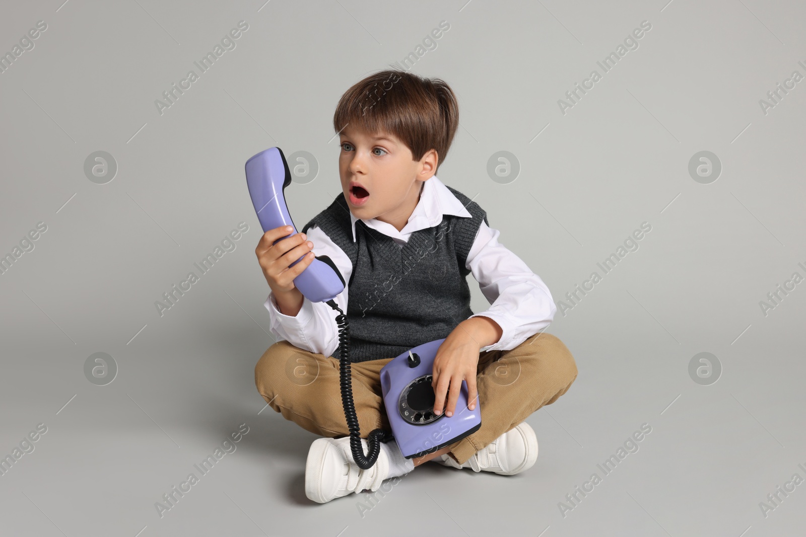 Photo of Cute little boy with old telephone on grey background