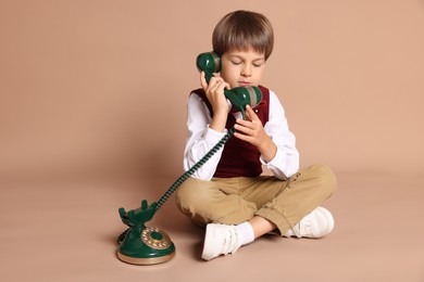 Photo of Cute little boy with old telephone on beige background