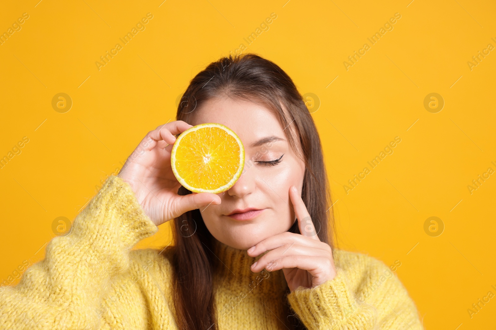 Photo of Young woman holding orange half near eye on orange background