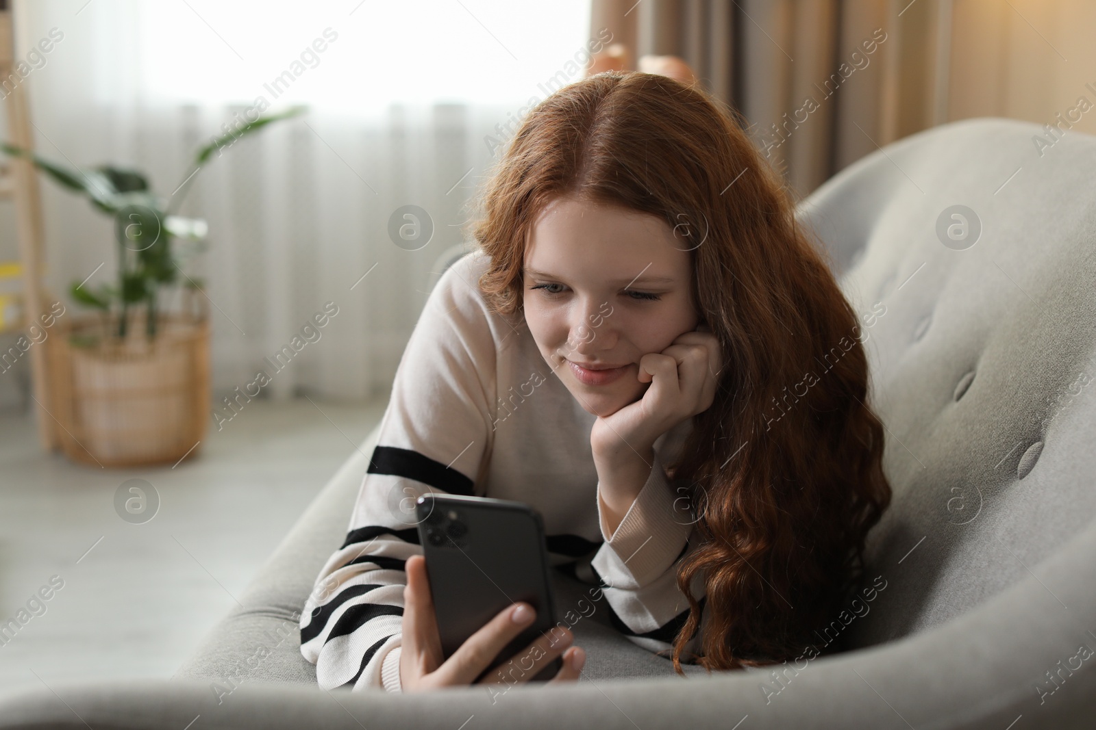 Photo of Beautiful teenage girl using smartphone on sofa at home