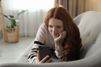 Beautiful teenage girl using smartphone on sofa at home