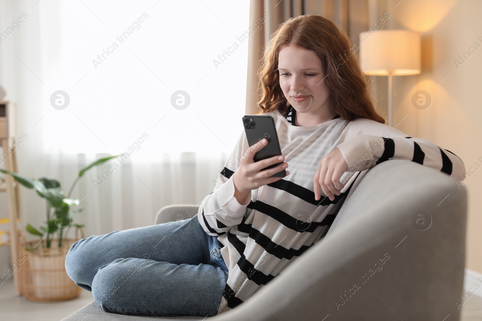 Photo of Beautiful teenage girl using smartphone on sofa at home