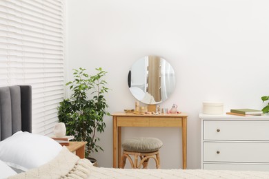 Photo of Mirror, dressing table, houseplant, bed and chest of drawers indoors. Interior design