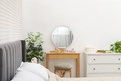 Photo of Mirror, dressing table, houseplant, bed and chest of drawers indoors. Interior design