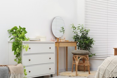 Photo of Mirror, dressing table, houseplants, stool and chest of drawers indoors. Interior design