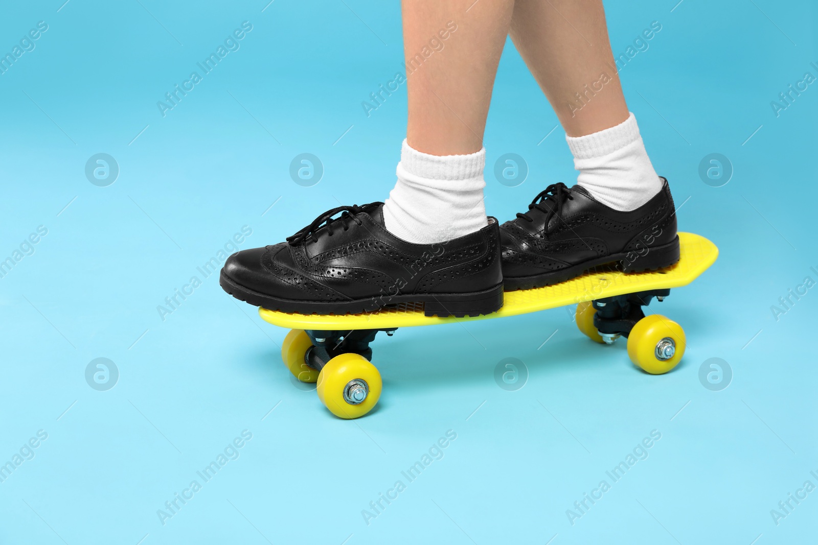 Photo of Little girl standing on penny board against light blue background, closeup