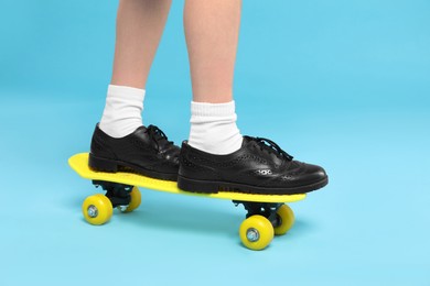 Photo of Little girl standing on penny board against light blue background, closeup