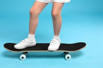 Photo of Little girl standing on skateboard against light blue background, closeup